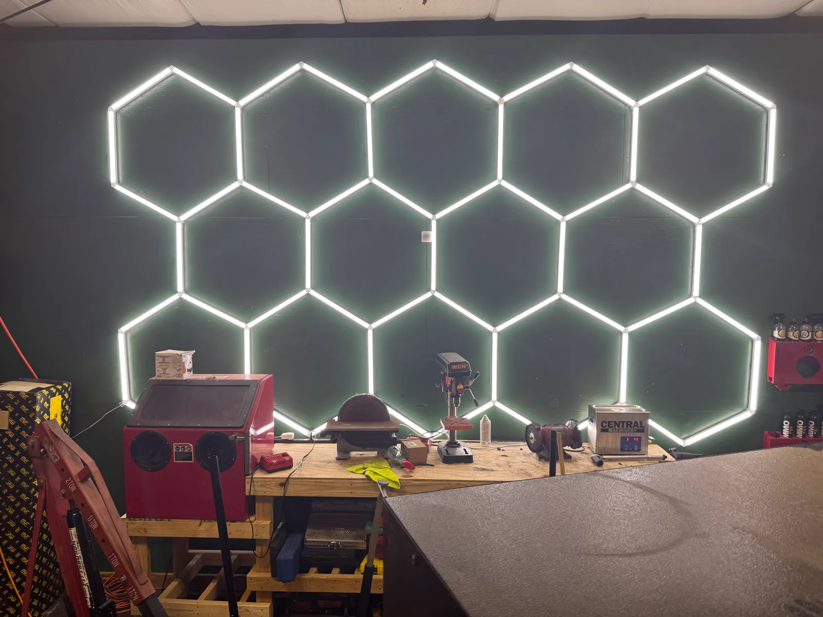 Hexagon LED lighting wall above the fabrication workbench: drill press, disc sander, bench grinder and blast cabinet.