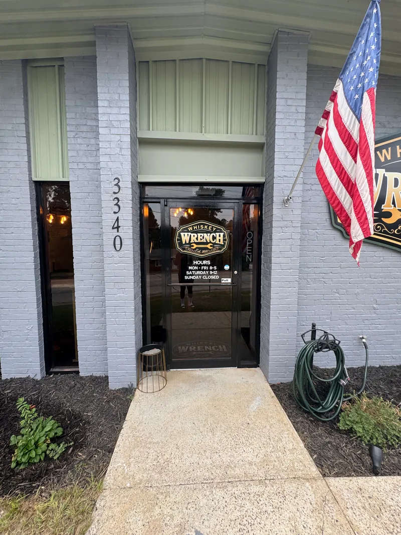 Front door with Whiskey Wrench decal and posted hours, American flag overhead.