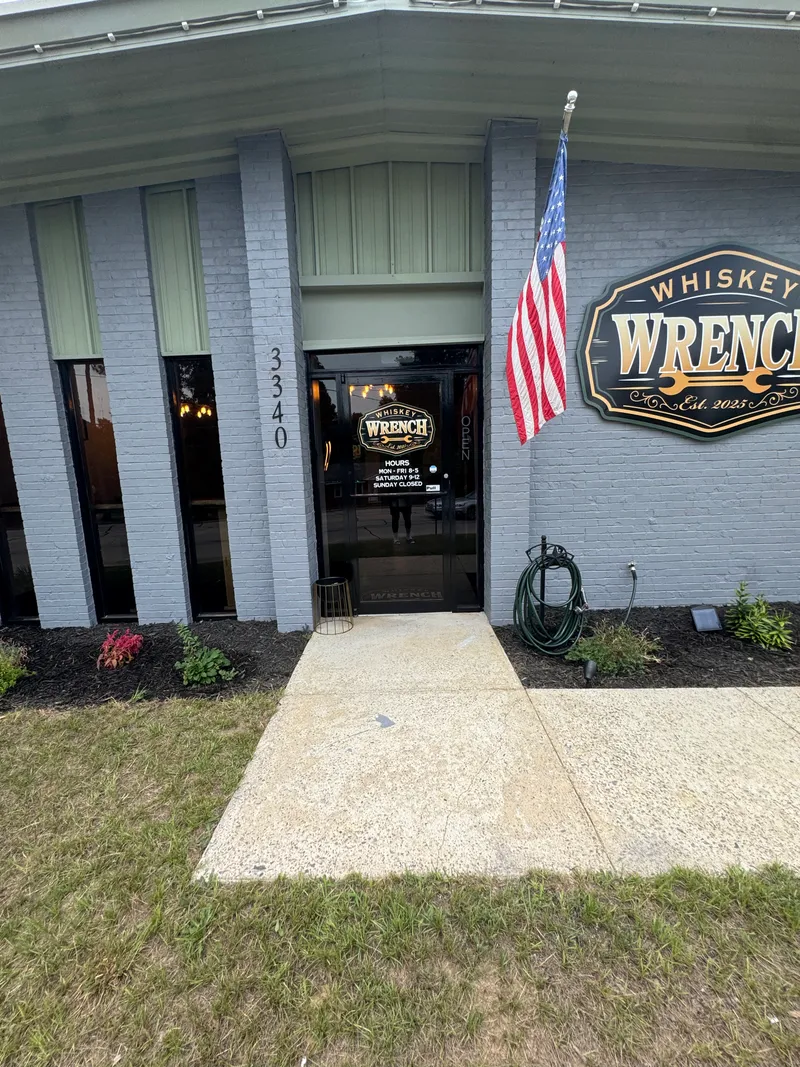 Whiskey Wrench entrance: gray brick, sage-green metal building, black and gold sign, American flag, number 3340.