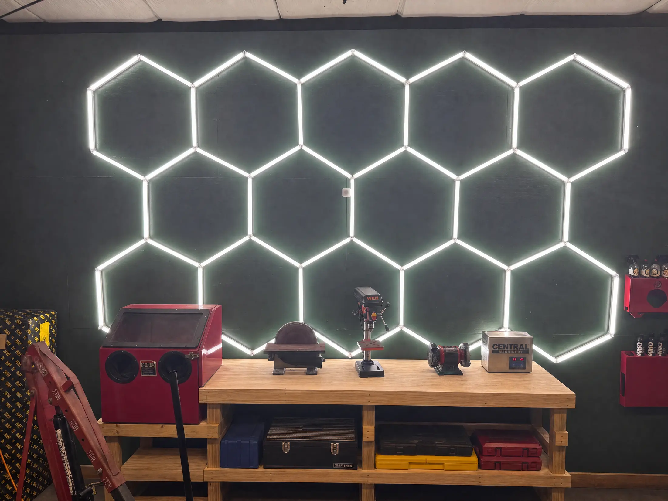The fabrication bench under the hexagon LED light wall: media blast cabinet, disc sander, drill press, bench grinder and ultrasonic parts cleaner.