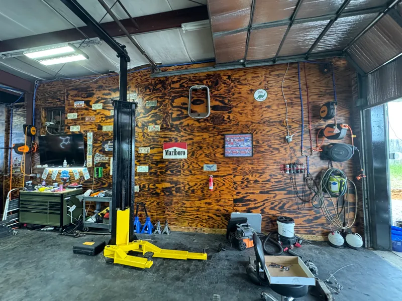 Burned-wood shop wall covered in vintage license plates, TV and single-post lift.