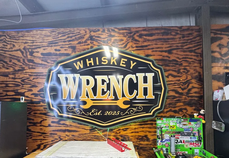 The Whiskey Wrench sign — black and gold whiskey-label badge on a burned-pine wall.