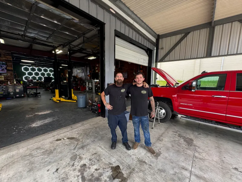 The two-man Whiskey Wrench crew at the bay door with a red Silverado 3500HD.